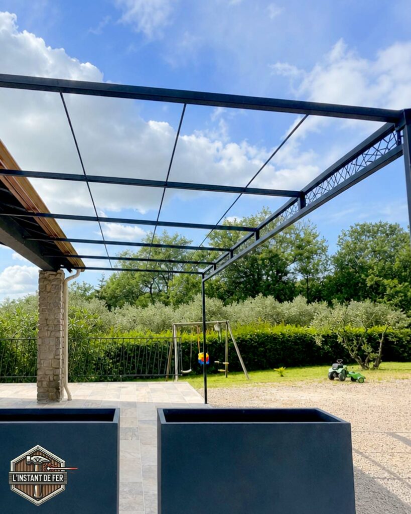 Pergola adossée avec traverse décorative en acier Grande pergola adossée en acier avec traverse décorative sur terrasse avec vue sur jardin