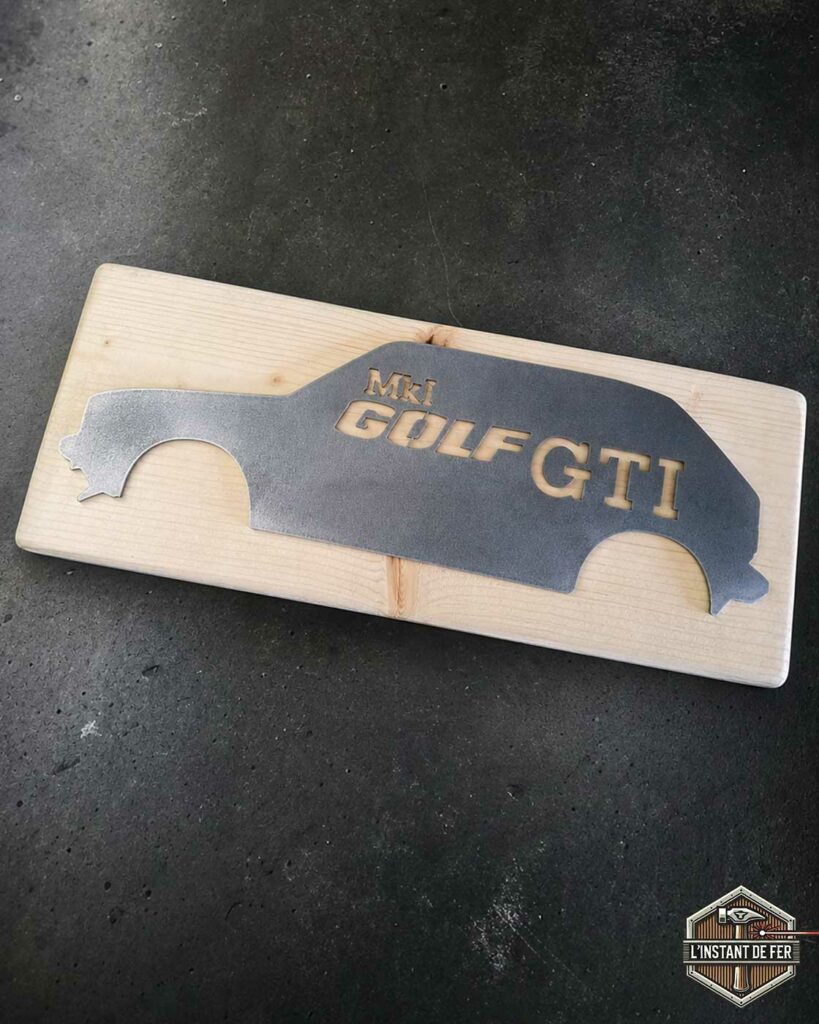 Silhouette golf gti mk1 decoration metal Décoration murale représentant la silhouette en métal d'une Golf GTI MK1 fixée sur un panneau en bois brut